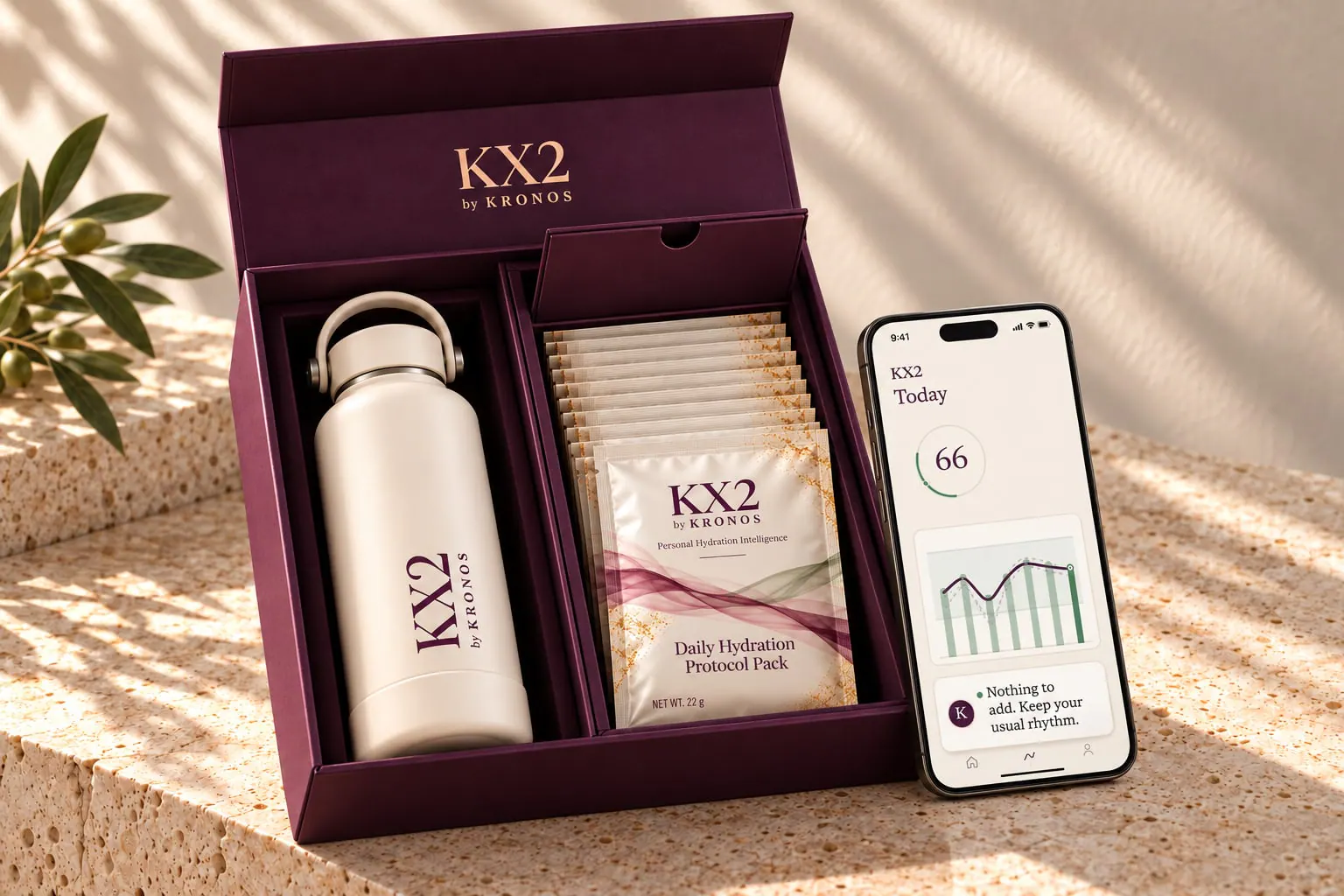 The KX2 system on a travertine ledge: the plum box open with the KX2 Bottle and a row of Daily Hydration Protocol Pack sachets, and a phone leaning against it showing the KX2 app — today's score, 66.